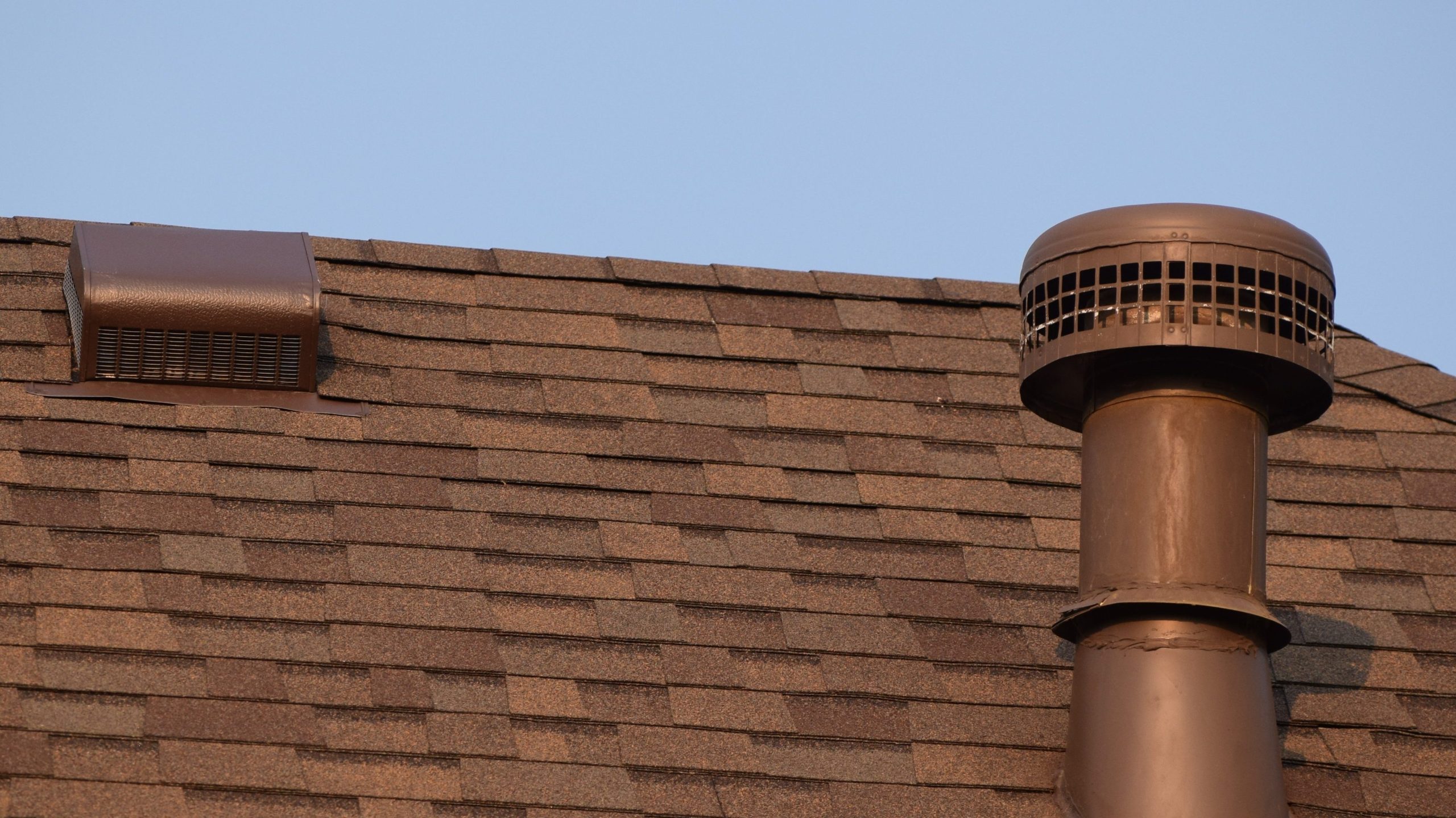 A box vent and a heater stack are pictured on a residential roof. 